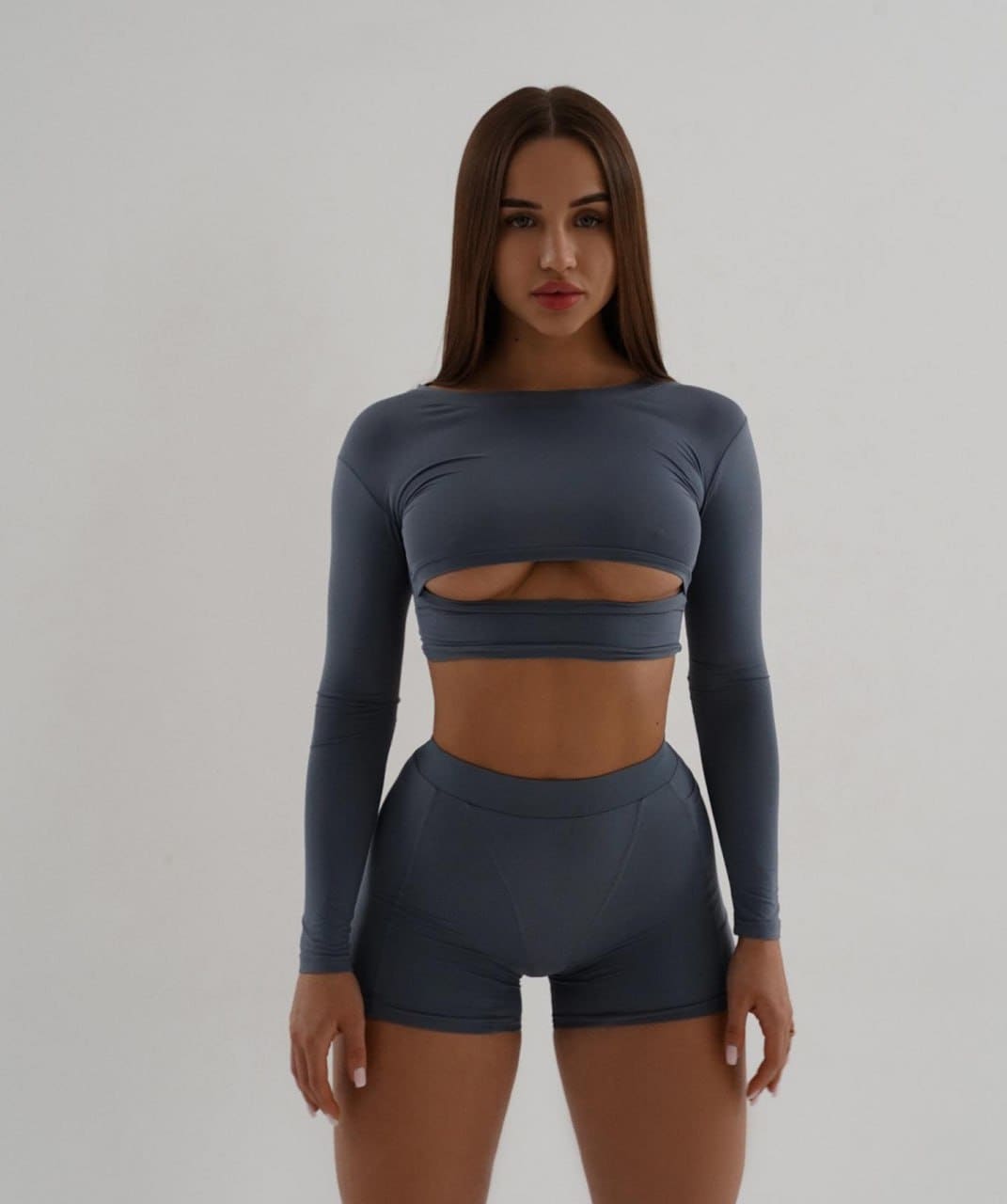 Aurora stands facing forward in a dark grey athletic crop top and shorts against a white background.