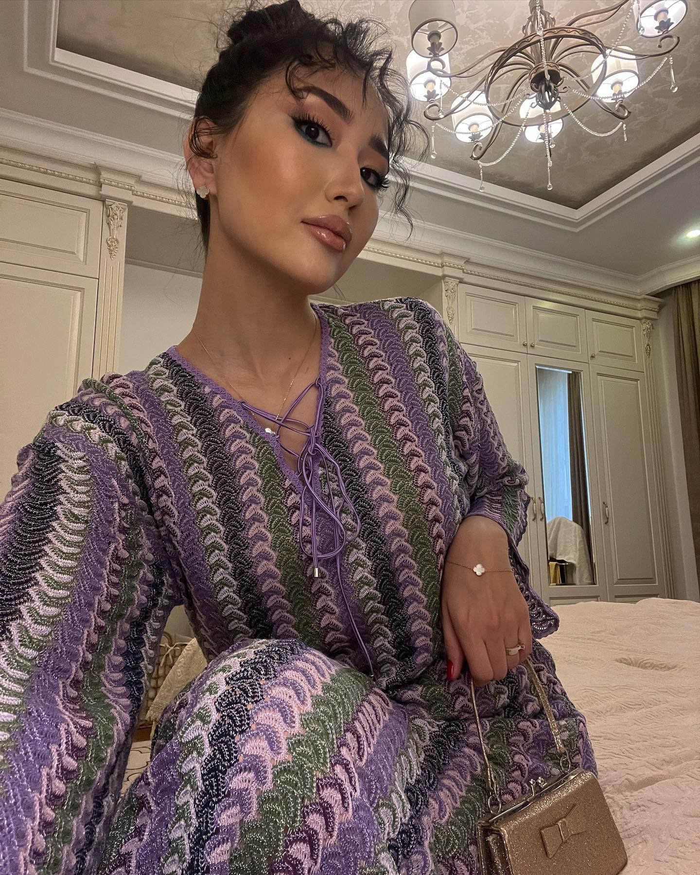 A woman in a sequined chevron dress sits on a bed holding a small metallic handbag.